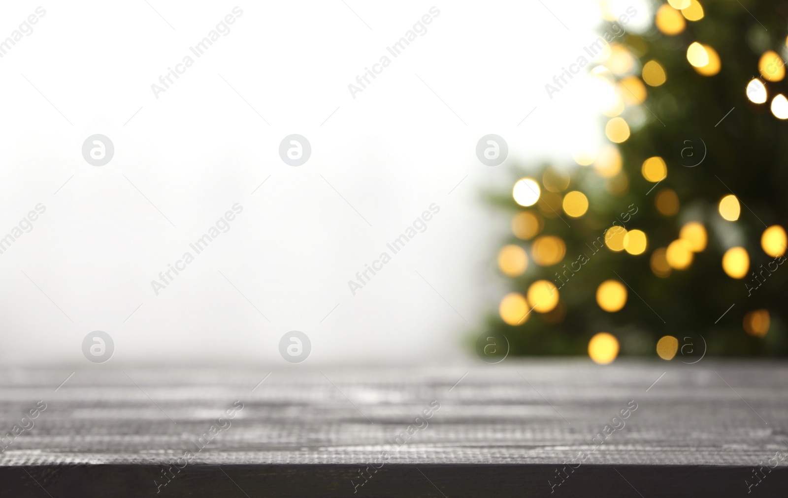 Photo of Empty table and blurred fir tree with yellow Christmas lights on background, bokeh effect. Space for design