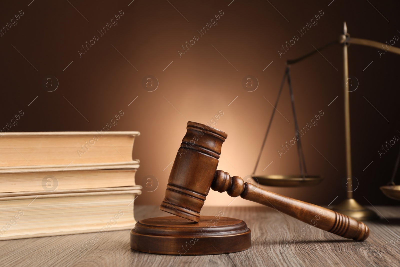 Photo of Judge's gavel with sound block, scales of justice and books on wooden table against brown background
