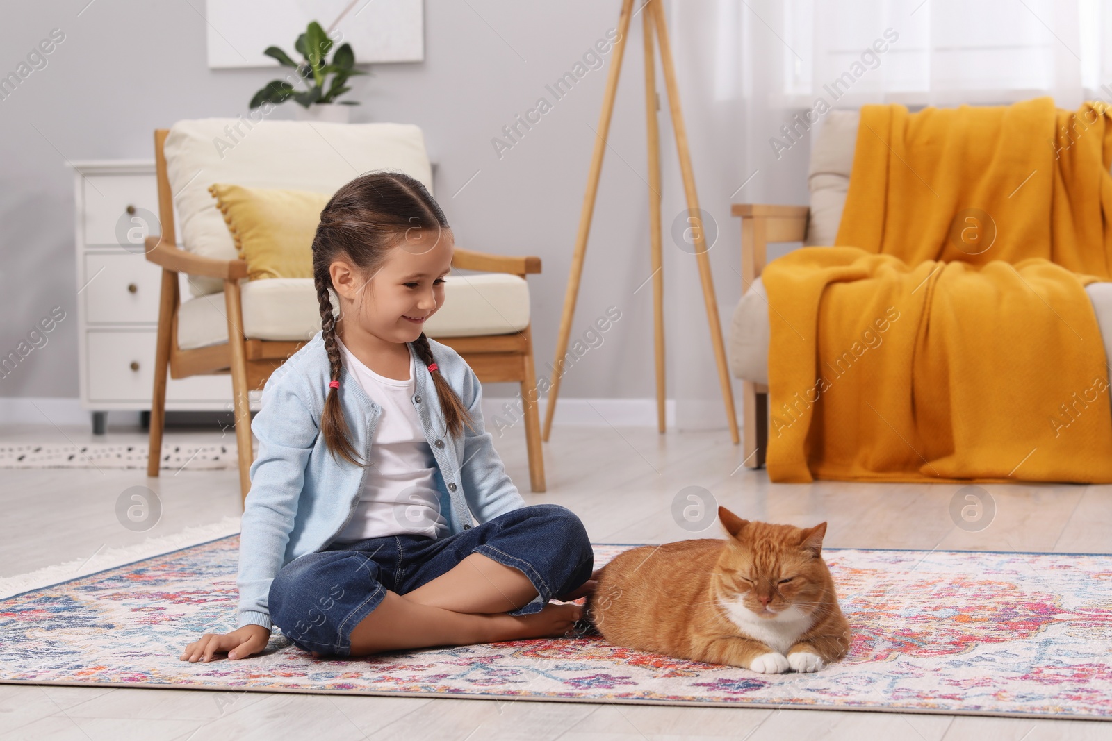 Photo of Happy little girl and cute ginger cat on carpet at home