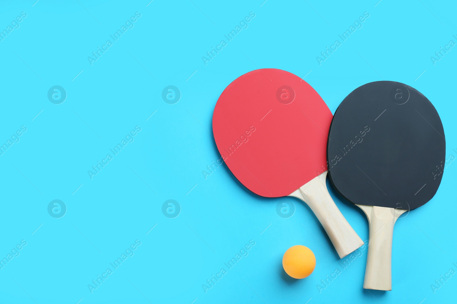 Photo of Ping pong rackets and ball on light blue background, flat lay. Space for text