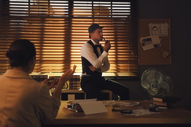 Photo of Old fashioned detective working with client in office