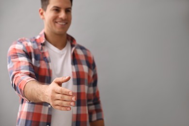 Photo of Man offering handshake against grey background, focus on hand. Space for text