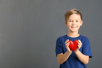 Photo of Cute boy holding wooden heart on grey background. Space for text