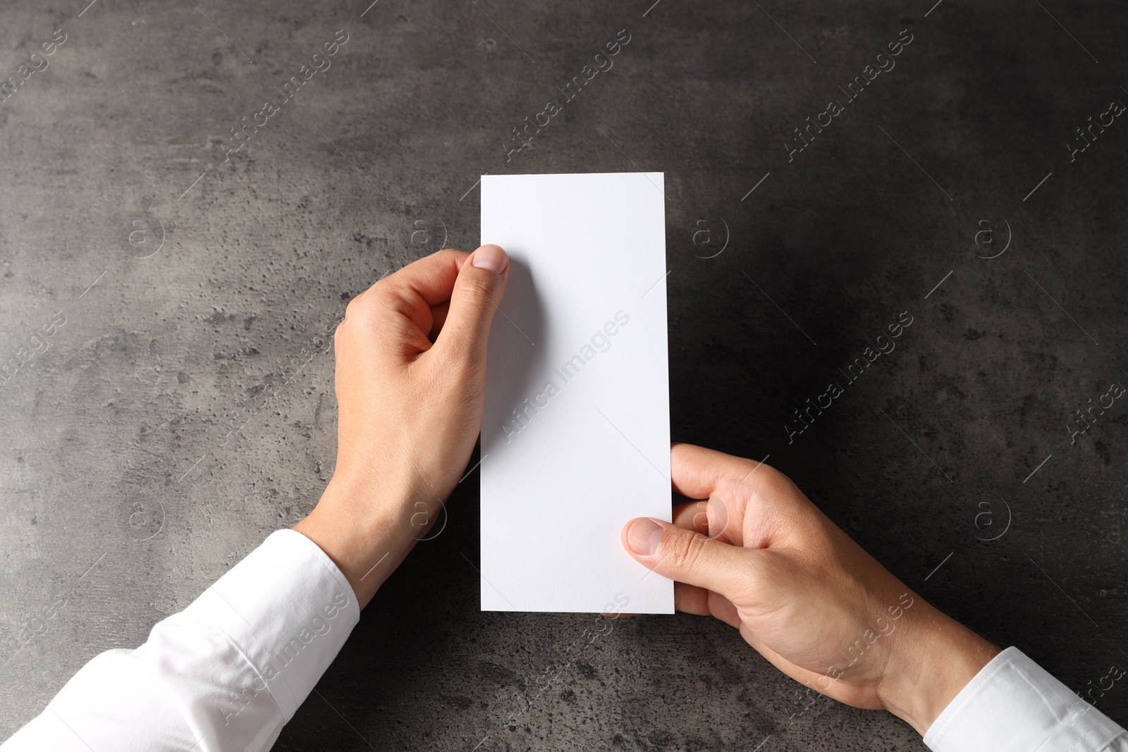 Photo of Man holding blank card at black textured table, top view. Mockup for design