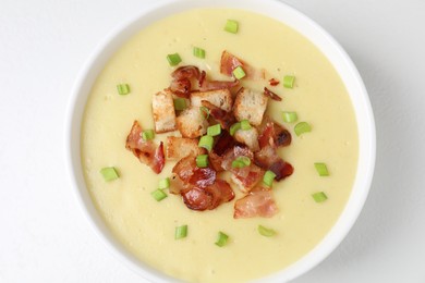 Tasty potato soup with bacon, green onion and croutons in bowl on white table, top view