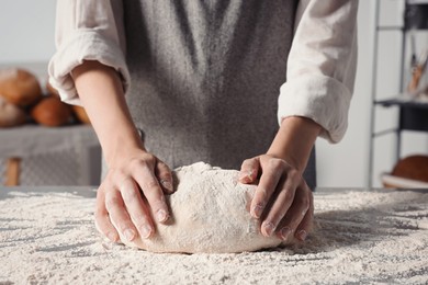 Photo of Woman kneading dough at table in kitchen, closeup