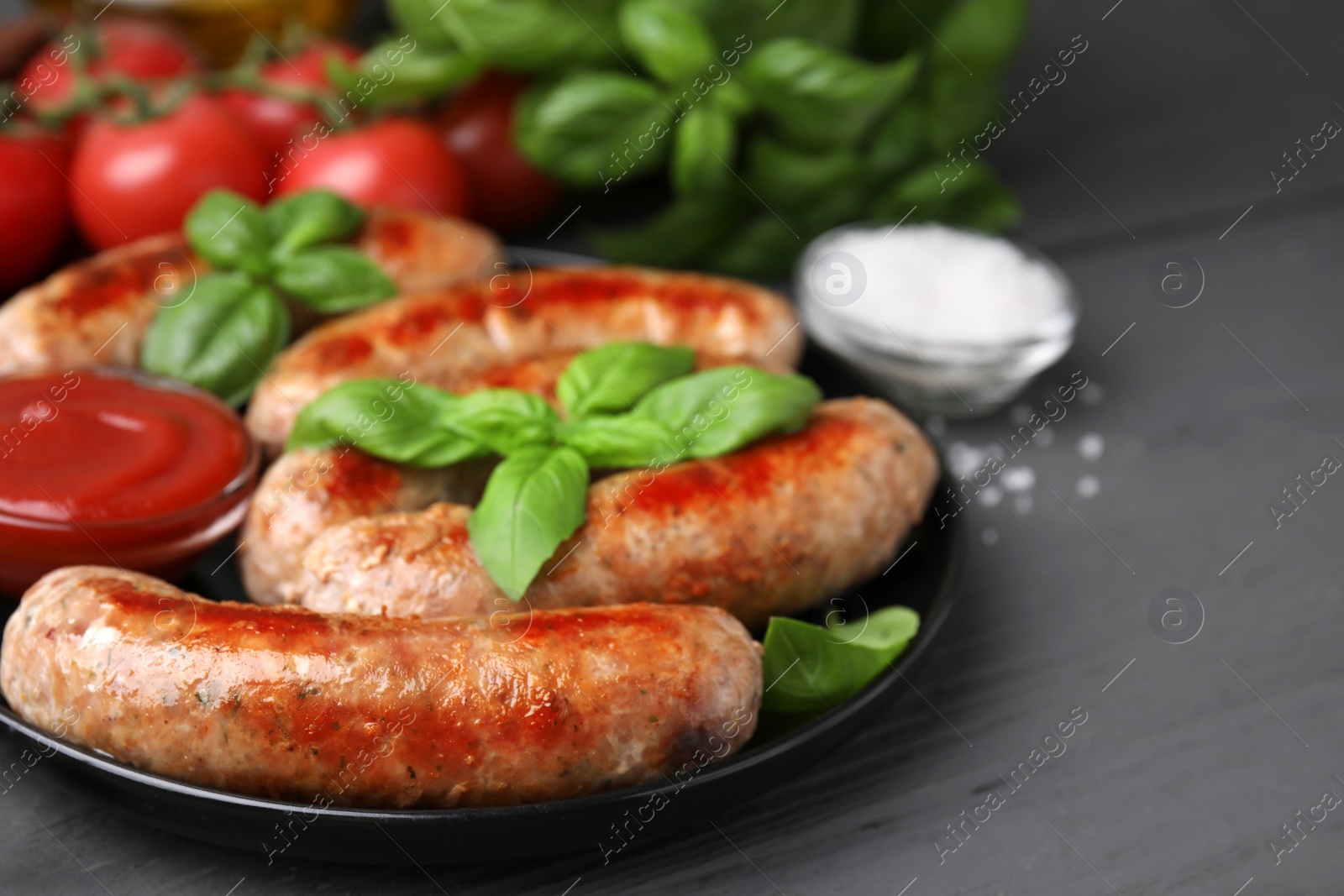 Photo of Tasty homemade sausages, ketchup and basil leaves on grey wooden table, closeup