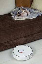 Photo of Robotic vacuum cleaner and cute Sphynx cat relaxing on sofa indoors