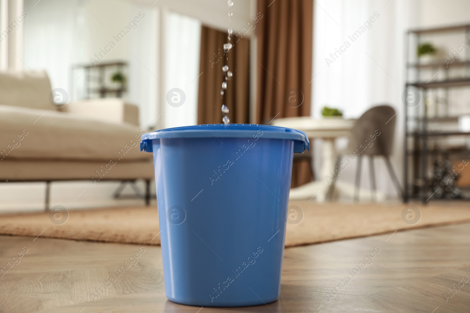 Photo of Bucket collecting water from ceiling in living room. Leaking roof