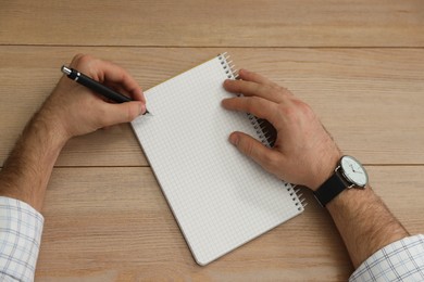 Photo of Left-handed man writing in notebook at wooden table, top view