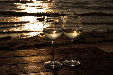 Photo of Two glasses of wine on wooden table near river at sunset