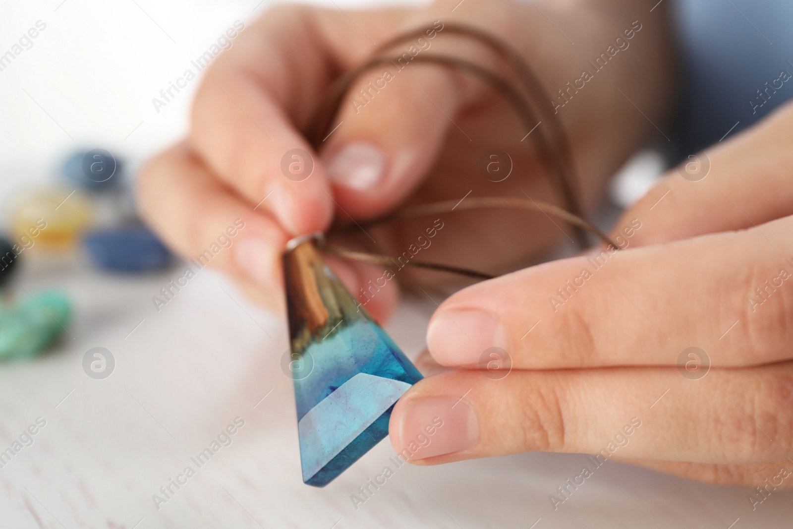 Photo of Woman holding handmade gemstone amulet at table, closeup