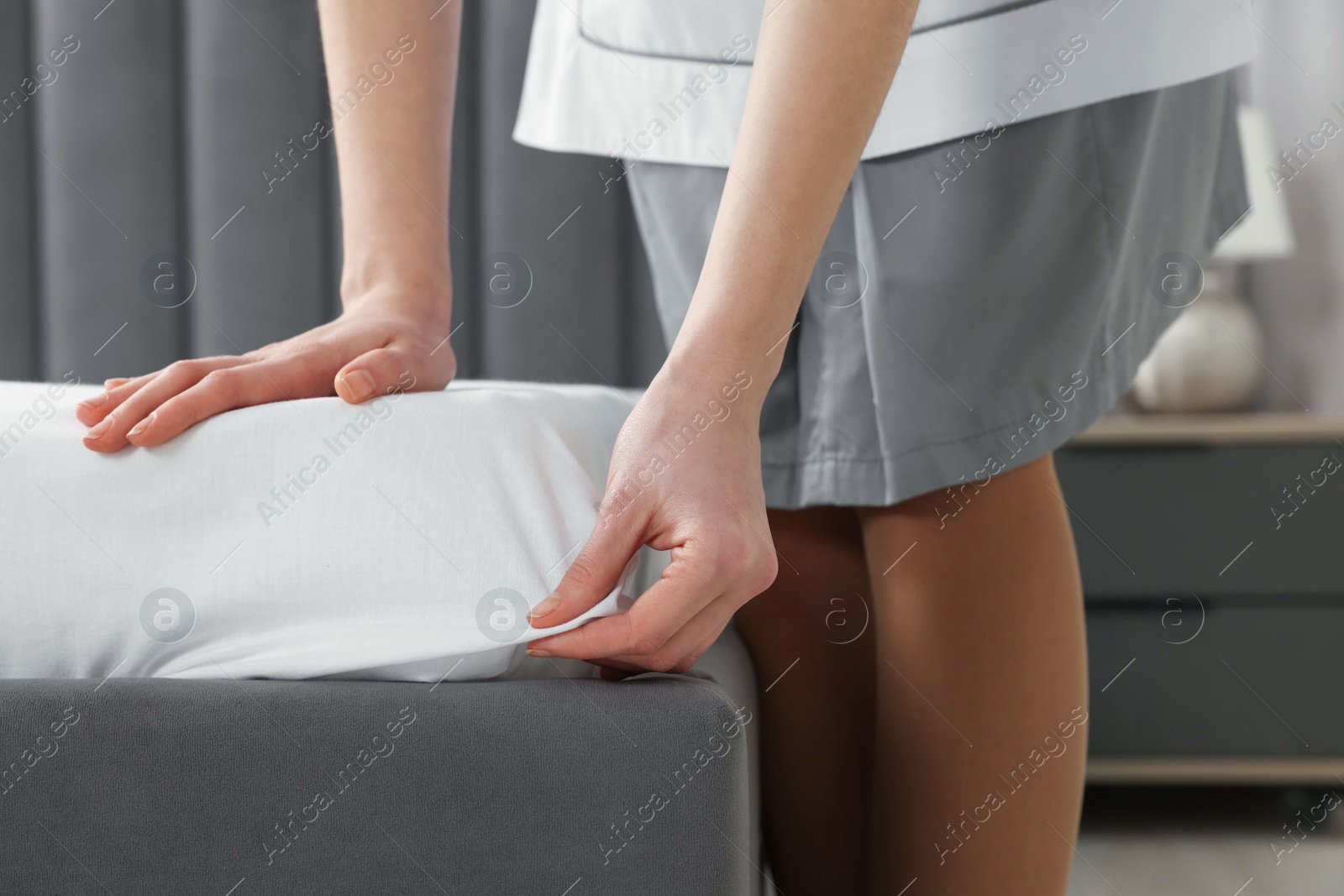 Photo of Young maid making bed in hotel room, closeup