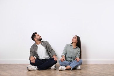 Photo of Young couple sitting on floor near white wall indoors