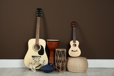 Photo of Set of different string and percussion musical instruments near brown wall indoors