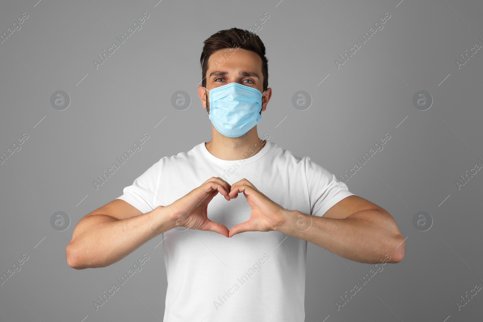 Photo of Man in protective mask making heart with hands on grey background