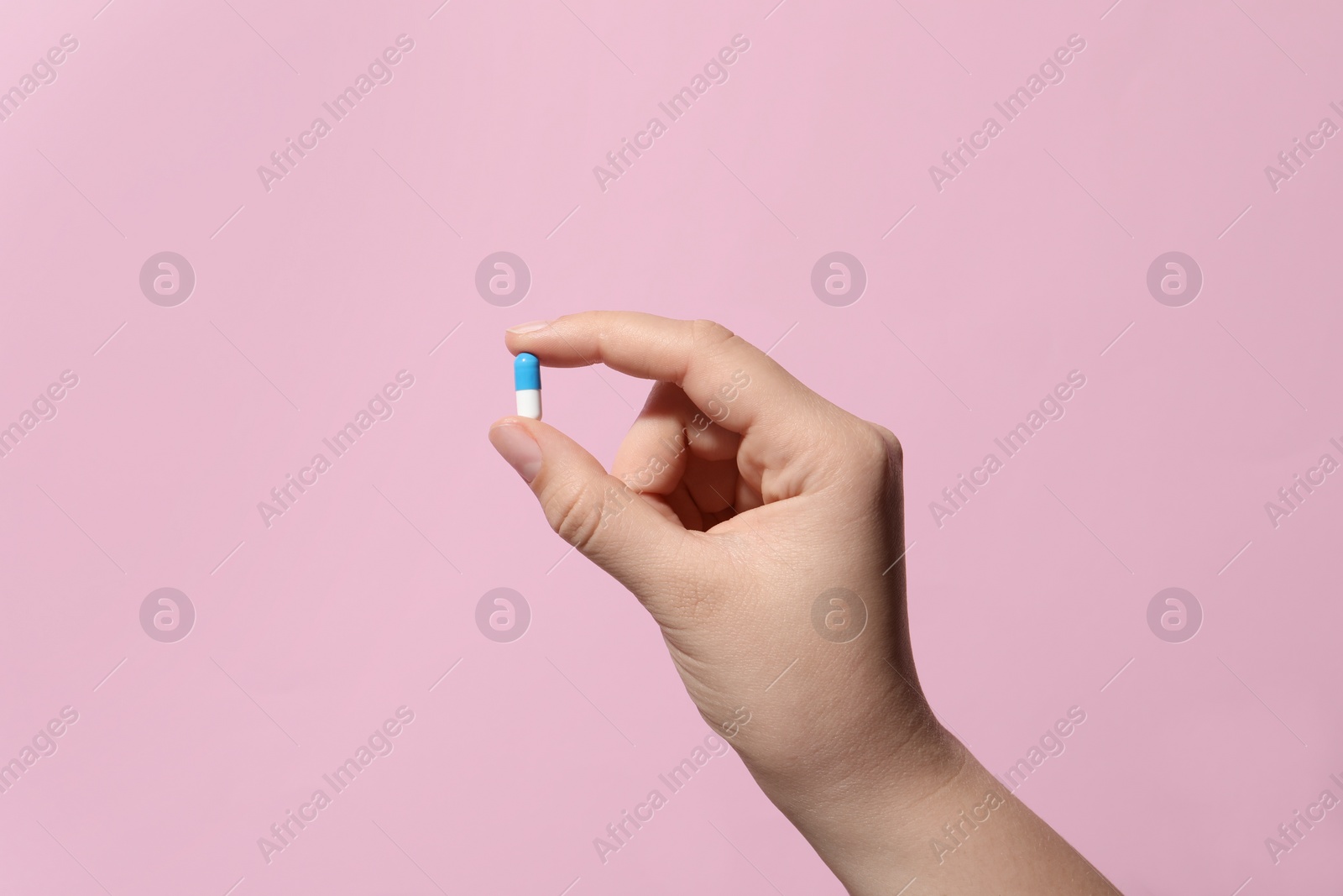 Photo of Woman holding pill on pink background, closeup