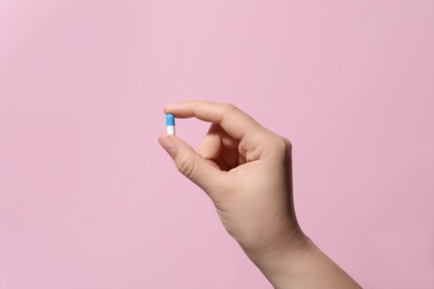 Photo of Woman holding pill on pink background, closeup