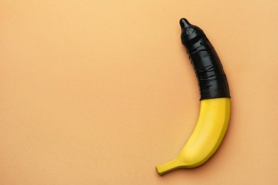 Photo of Banana with condom on pale orange background, top view and space for text. Safe sex concept