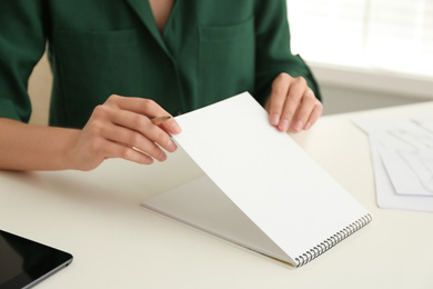 Photo of Woman with pencil and notepad at white table, closeup