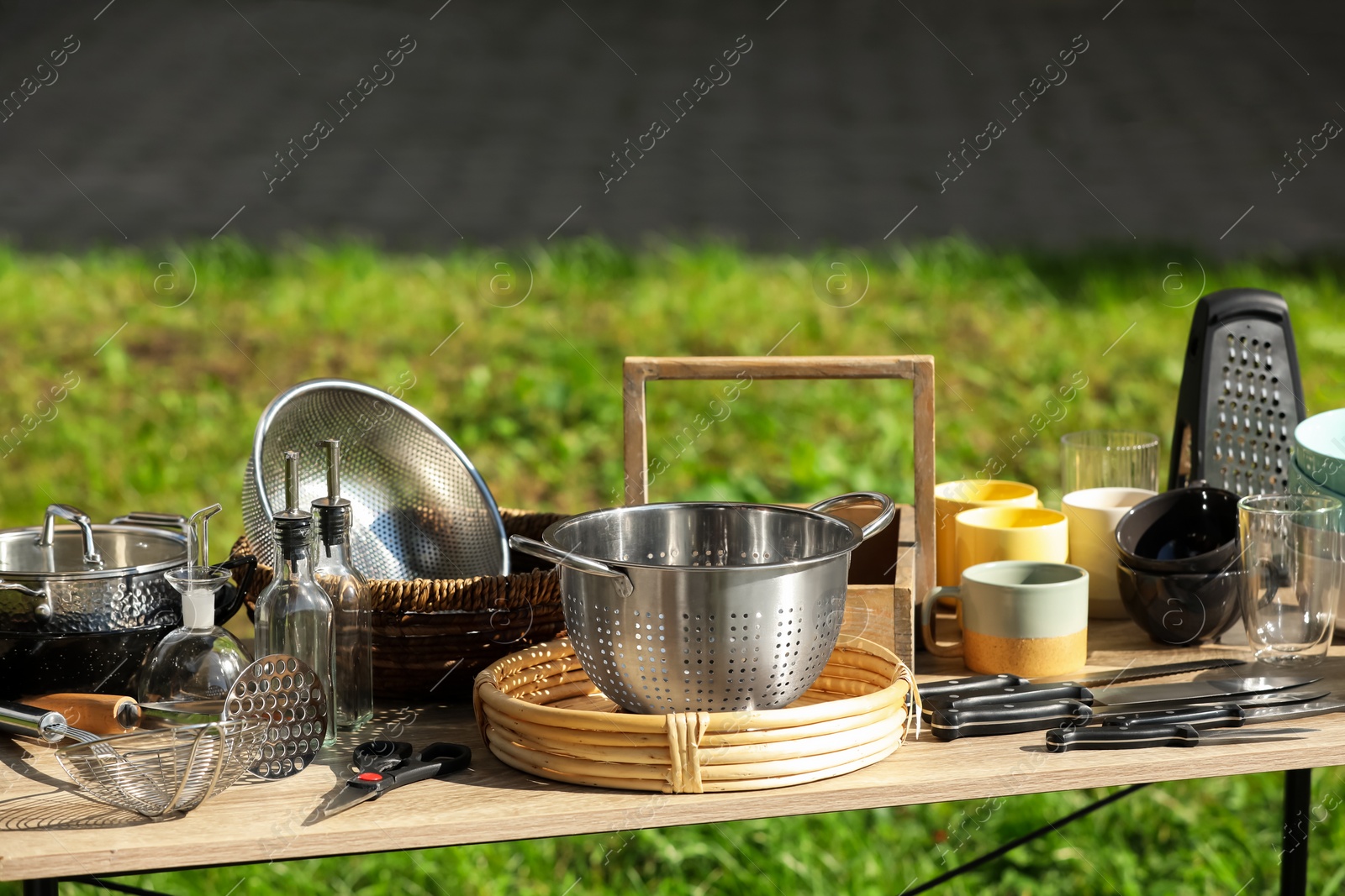 Photo of Many different kitchen items on wooden table outdoors. Garage sale