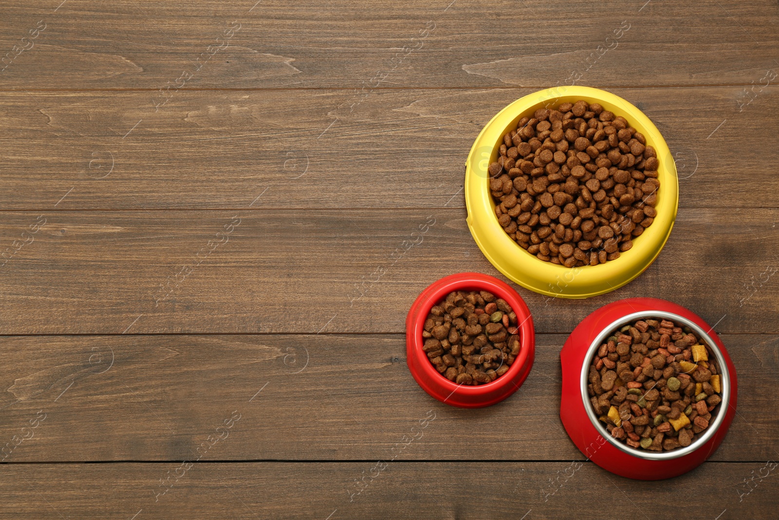 Photo of Dry food in pet bowls on wooden background, flat lay. Space for text