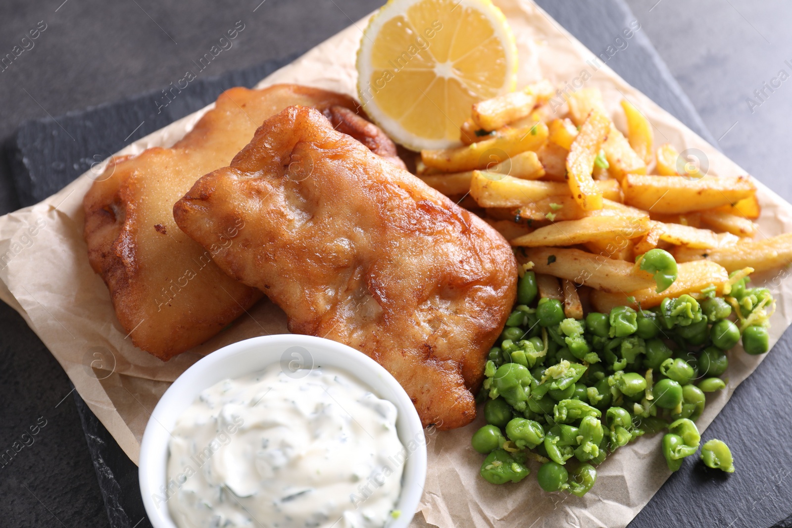 Photo of Tasty fish, chips, sauce and peas on grey table, closeup