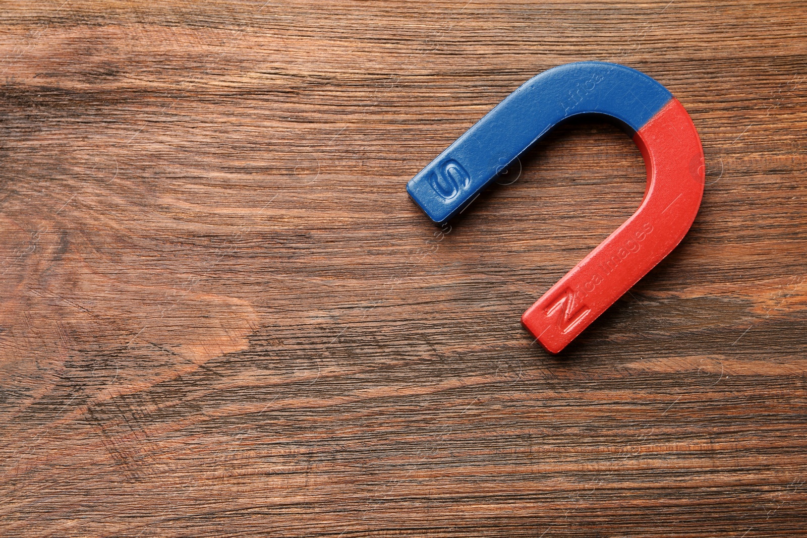 Photo of Red and blue horseshoe magnet on wooden background, top view with space for text