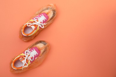 Photo of Women's sneakers in shoe covers on coral background, top view. Space for text