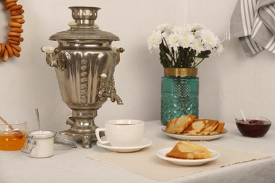 Vintage samovar, cup of hot drink and snacks served on table indoors. Traditional Russian tea ceremony