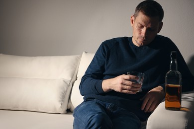 Photo of Addicted man with alcoholic drink on sofa indoors. Space for text