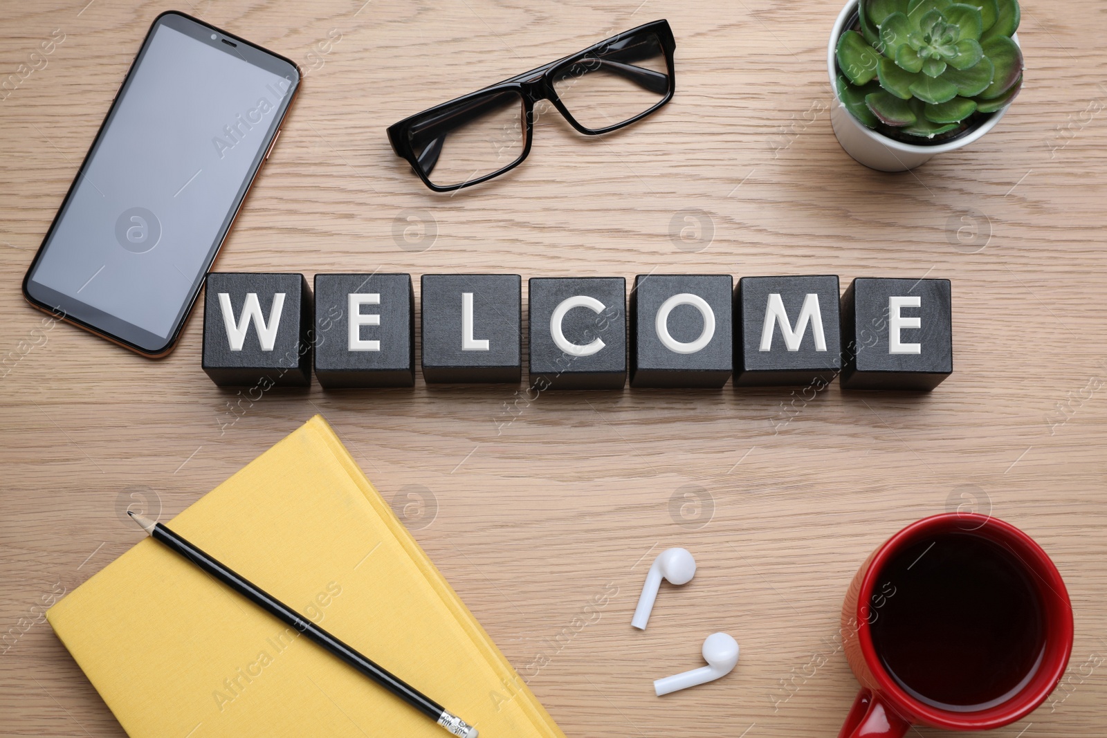 Photo of Word WELCOME made with black cubes, cup of coffee and smartphone on wooden table, flat lay