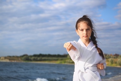 Cute little girl in kimono practicing karate near river