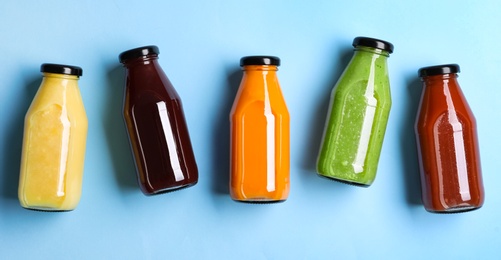 Bottles with delicious colorful juices on light blue background, flat lay