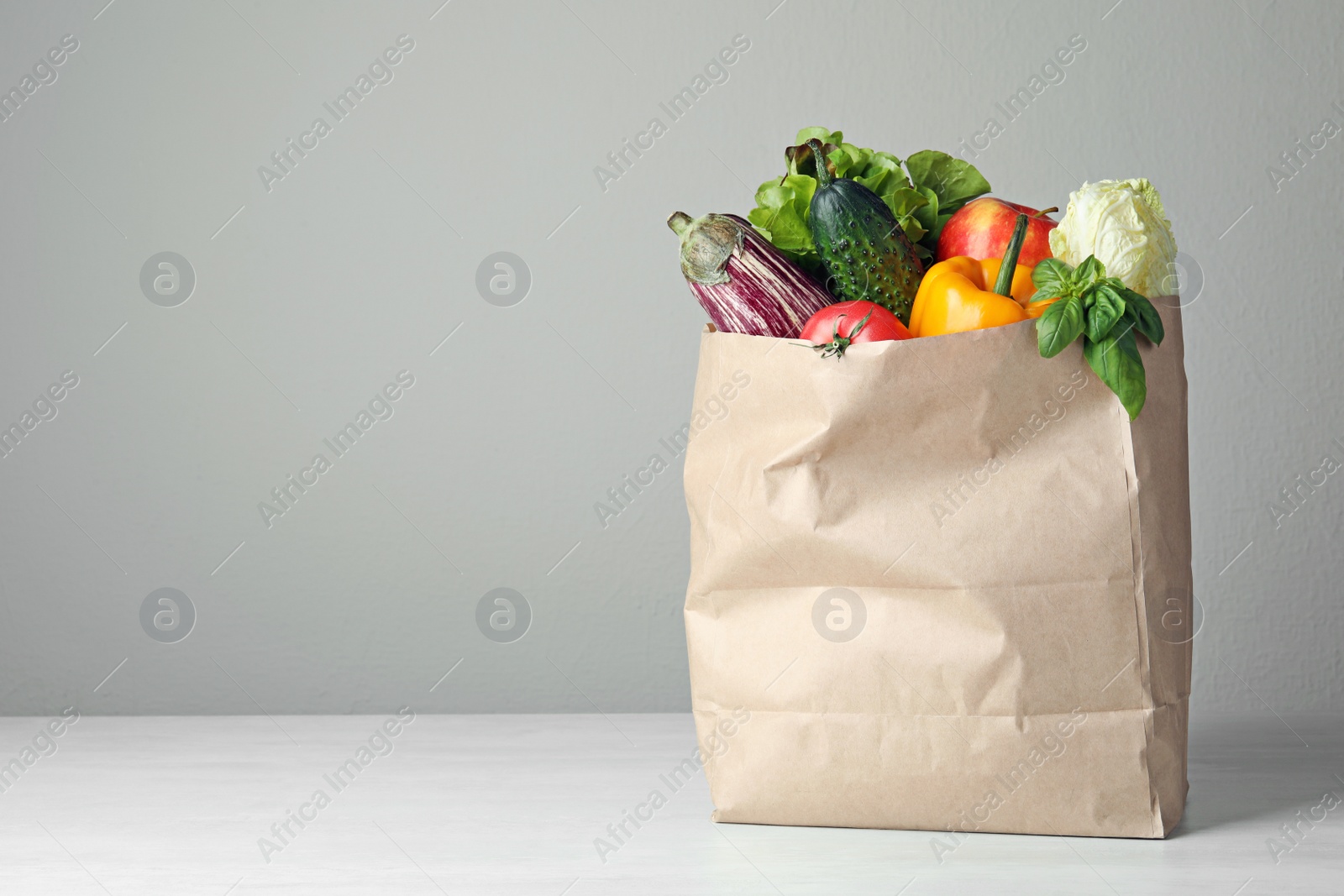 Photo of Paper bag with vegetables on table against grey background. Space for text