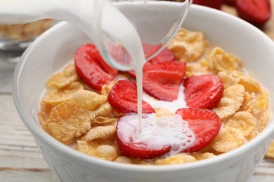 Photo of Pouring milk into bowl of tasty crispy corn flakes with strawberries at table, closeup
