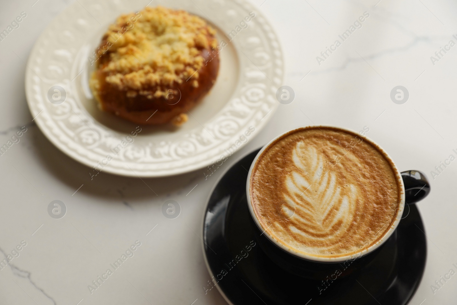 Photo of Cup of fresh coffee and bun on white marble table, above view