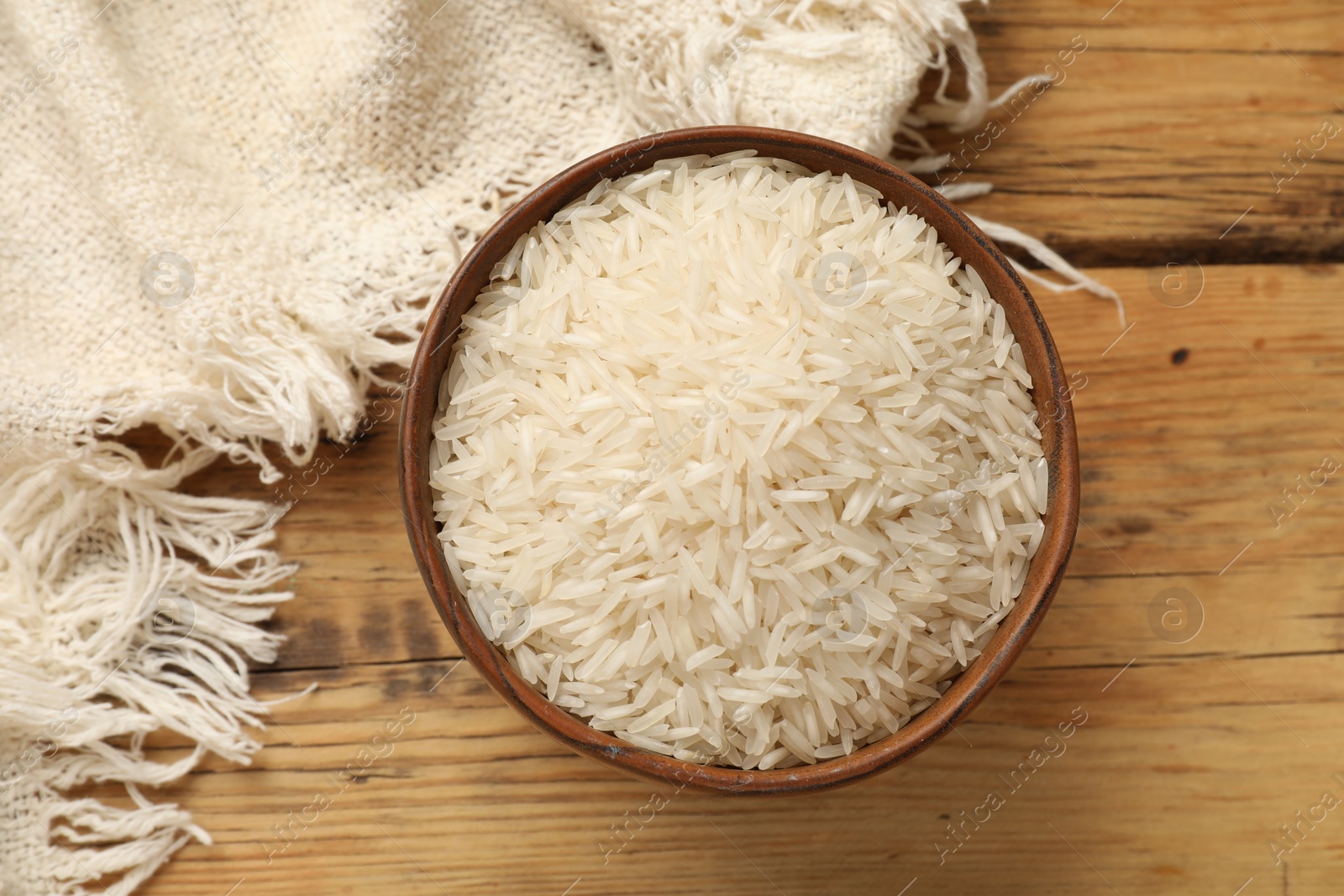 Photo of Raw basmati rice in bowl on wooden table, top view