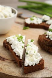 Photo of Bread with cottage cheese and green onion on wooden board, closeup