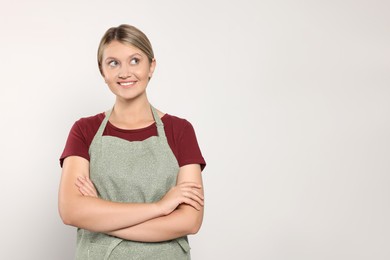 Photo of Beautiful young woman in clean apron on light grey background. Space for text