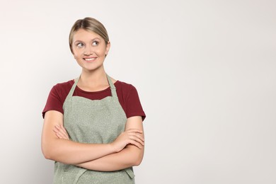 Beautiful young woman in clean apron on light grey background. Space for text