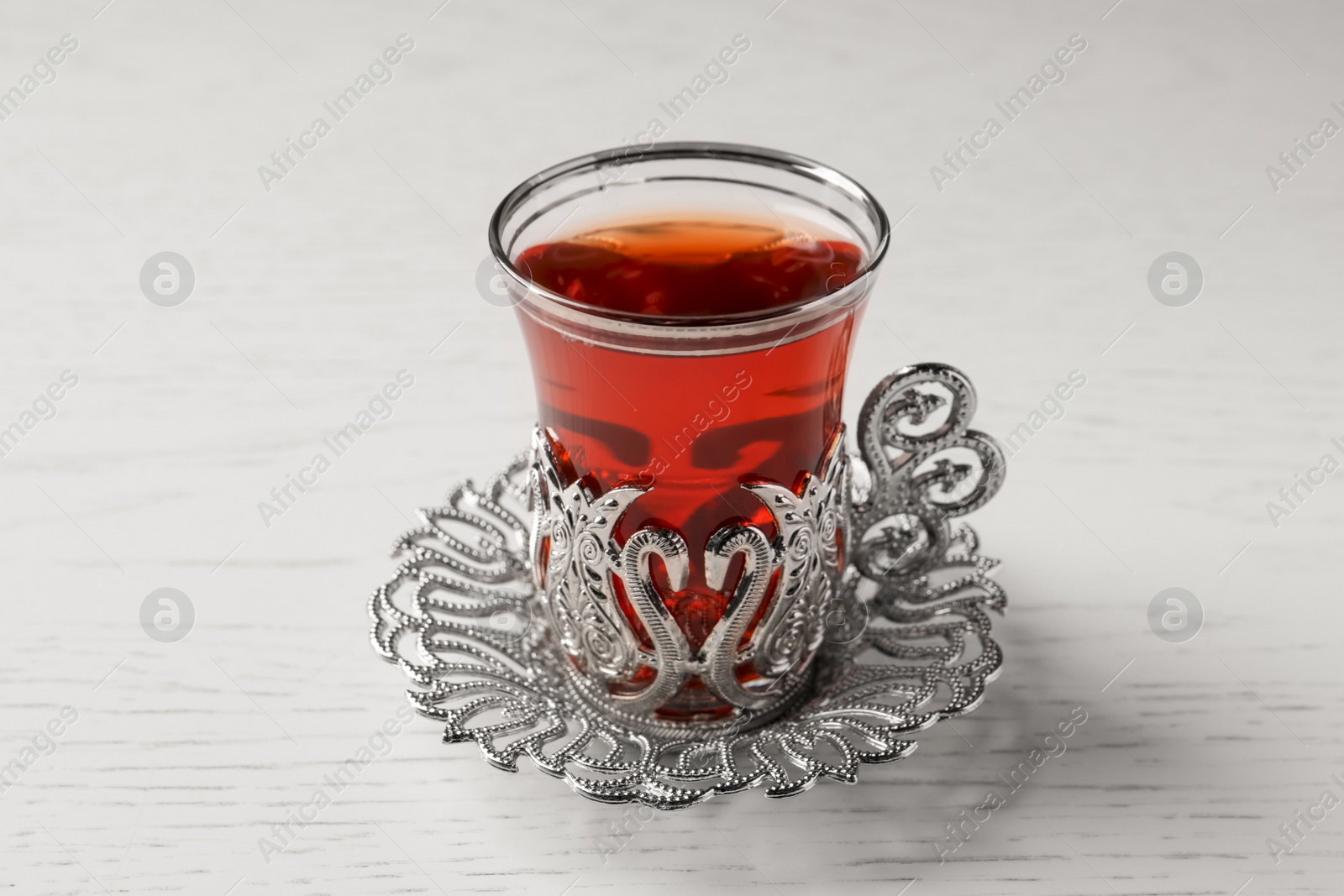 Photo of Glass of traditional Turkish tea in vintage holder on white wooden table, closeup