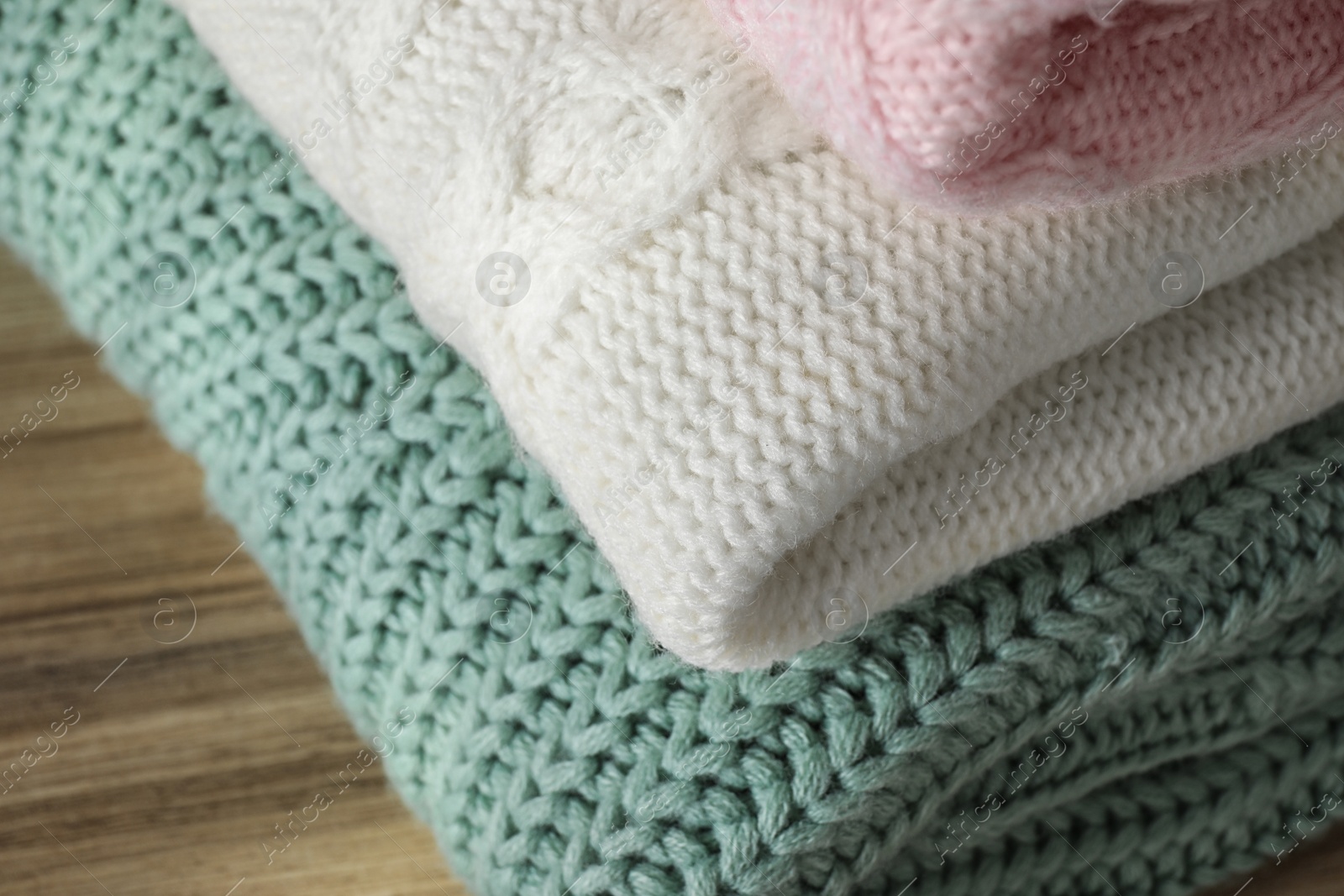 Image of Stack of folded warm sweaters on wooden table, closeup