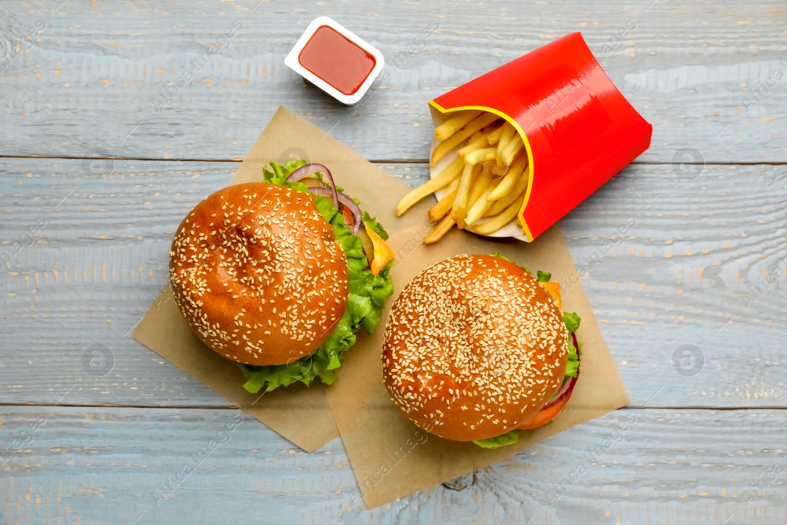 Photo of French fries, burgers and ketchup on grey wooden table, flat lay. Fast food