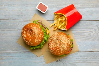 Photo of French fries, burgers and ketchup on grey wooden table, flat lay. Fast food