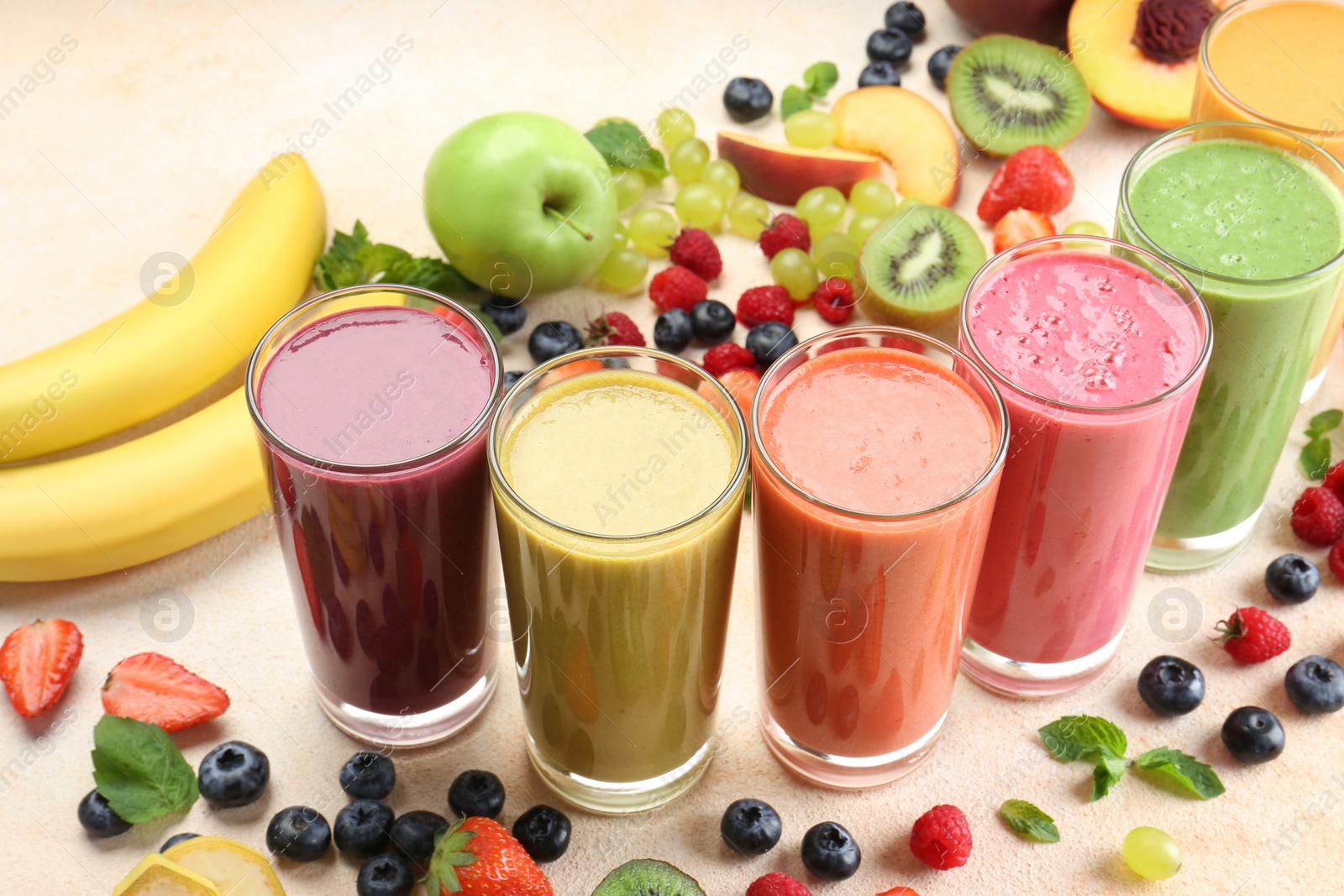 Photo of Fresh colorful fruit smoothies and ingredients on beige table