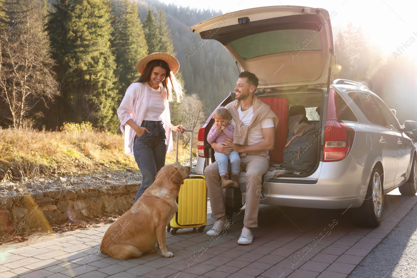 Photo of Parents, their daughter and dog near car outdoors. Family traveling with pet