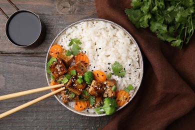 Photo of Delicious rice with fried tofu, broccoli and carrots served on wooden table, flat lay