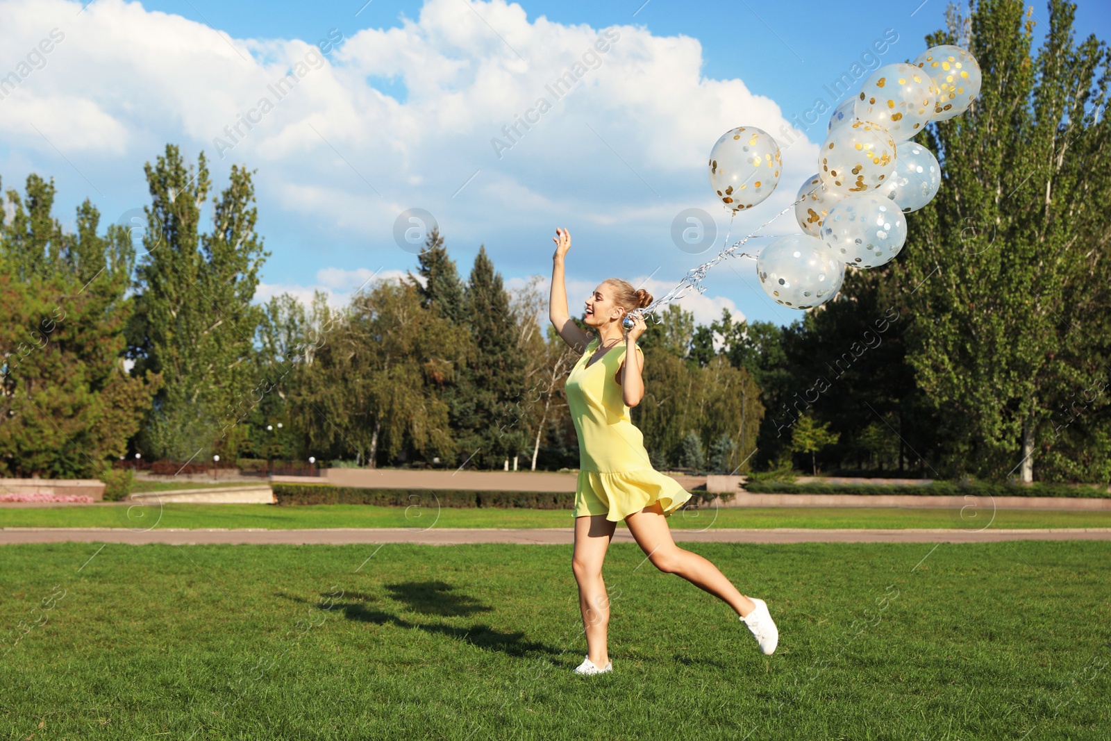 Photo of Beautiful young woman holding glitter balloons in park