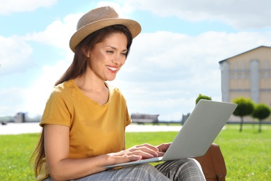 Beautiful woman with laptop sitting on green lawn outdoors